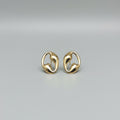 A pair of polished gold-toned abstract loop stud earrings resting on a glossy white ceramic surface, with a bamboo slat background.